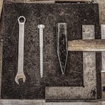 A collection of vintage workshop tools including a wrench, nail, and hammer displayed on a wooden table.
